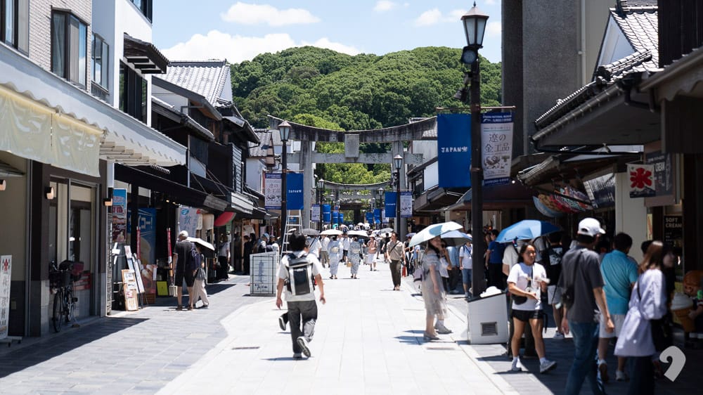 Busy pedestrian shopping street leading to Dazaifu Tenmangu Shrine with visitors and stone torii gate