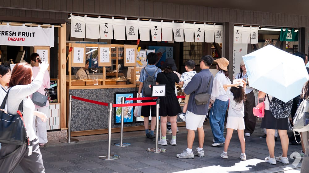 Tourists queuing in front of a popular food counter with white noren curtains in Dazaifu