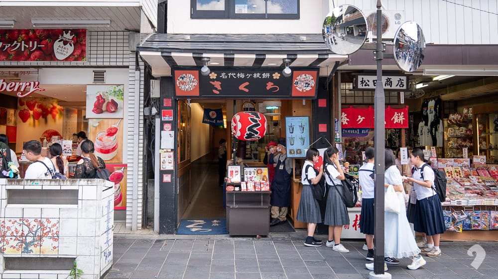 raditional storefront with red lanterns and students walking past on a Dazaifu street