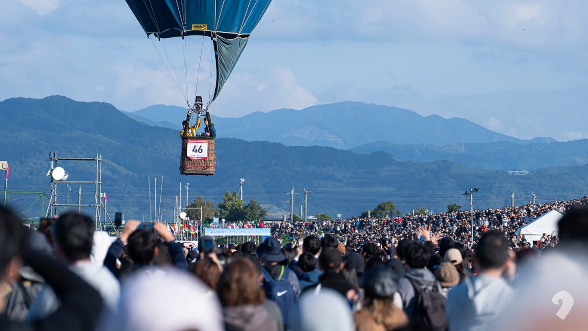 佐賀熱氣球節現場，載着乘客的熱氣球吊籃從密集的觀眾人群上方飛過
